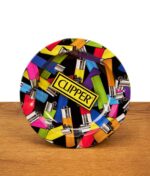 Runder Clipper Aschenbecher mit buntem Feuerzeug-Allover-Print und gelbem Clipper-Logo steht auf einer Holzoberfläche vor weißem Hintergrund.