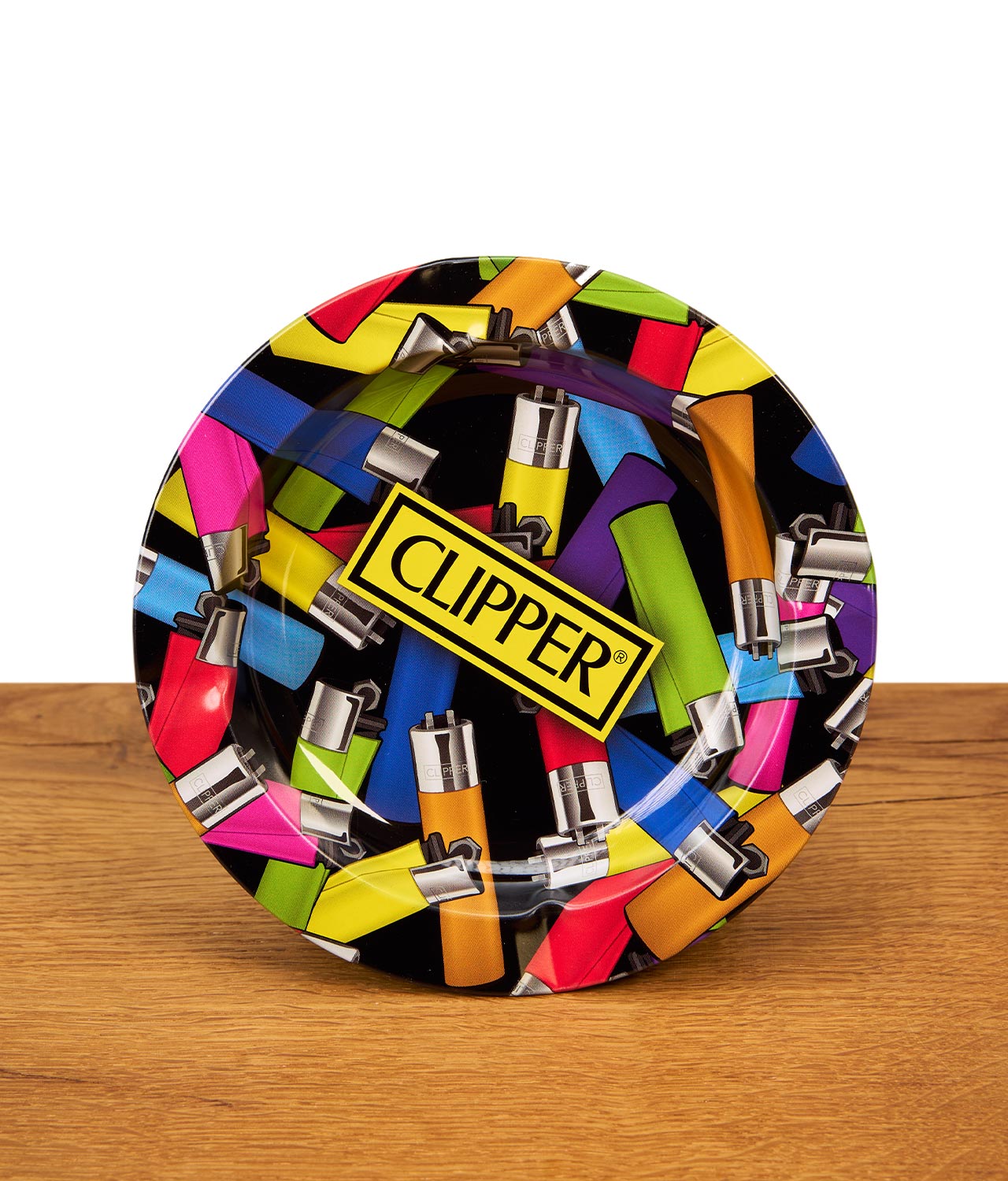 fire-flow-clipper-chaos-aschenbecher-jpg Runder Clipper Aschenbecher mit buntem Feuerzeug-Allover-Print und gelbem Clipper-Logo steht auf einer Holzoberfläche vor weißem Hintergrund.