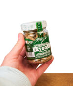 Hand hält ein Purize Glas mit braunen Organic Aktivkohlefiltern über einer Holzoberfläche vor weißem Hintergrund.