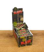 RAW Black Organic Rolls King Size 12er Pack-Display-Box steht aufrecht auf einer Holzoberfläche vor weißem Hintergrund, mehrere einzelne Pakete in der aufklappbaren Schublade sichtbar, schwarze Verpackung mit organischem Hanfsiegel oben.