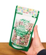 Hand hält eine grüne Purize 100er Pack Regular Size Verpackung mit buntem Aktivkohlefilter-Muster vor weißem Hintergrund über einer Holzoberfläche.