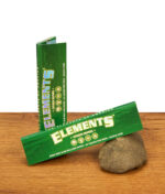 Geöffnetes Heftchen Elements Green Papers auf einem Stein vor einer hochkant stehenden Verpackung