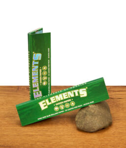 Geöffnetes Heftchen Elements Green Papers auf einem Stein vor einer hochkant stehenden Verpackung