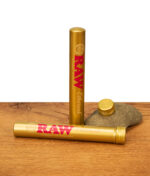 Zwei goldene RAW Ethereal Jointtubes aus Aluminium, eine stehend und eine liegend mit abgeschraubtem Deckel auf einem Naturstein.