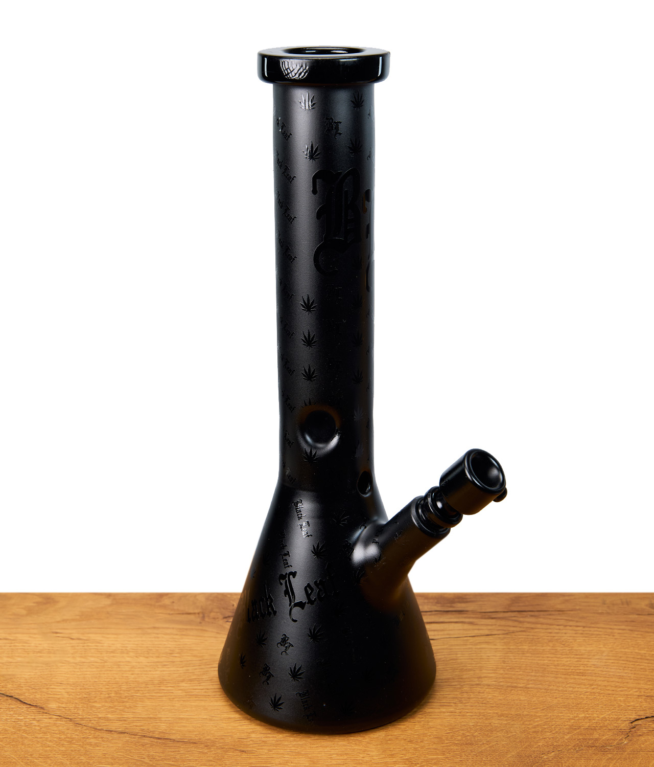 black-leaf-beakerbong-1-jpg Schwarze Black Leaf Beakerbong mit eingravierten Hanfblättern und Schriftzug, seitliche Ansicht auf Holztisch.