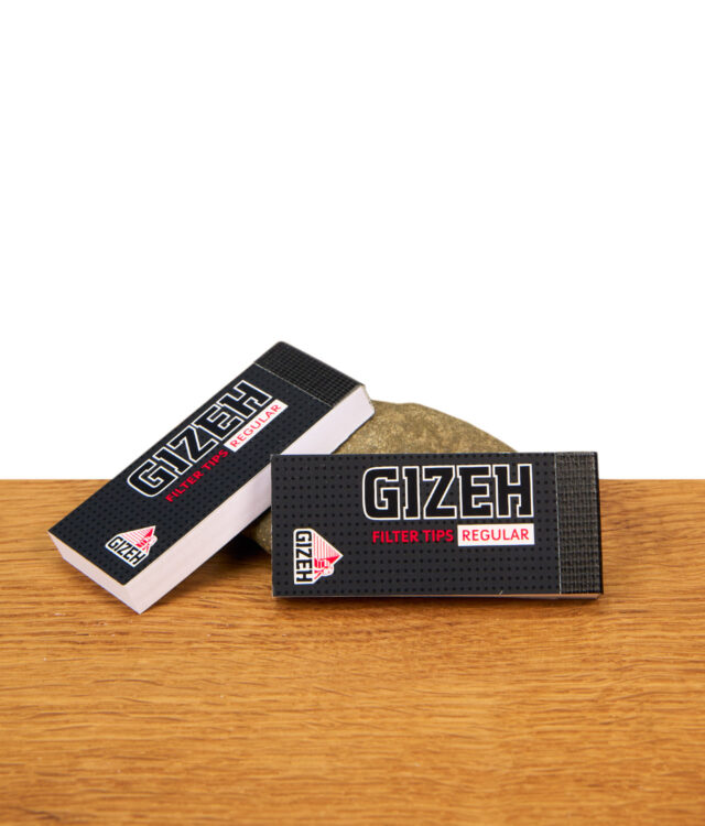Zwei Packungen Gizeh Regular Filter Tips im schwarzen Design mit Logo auf einer Holzoberfläche vor einem Stein.