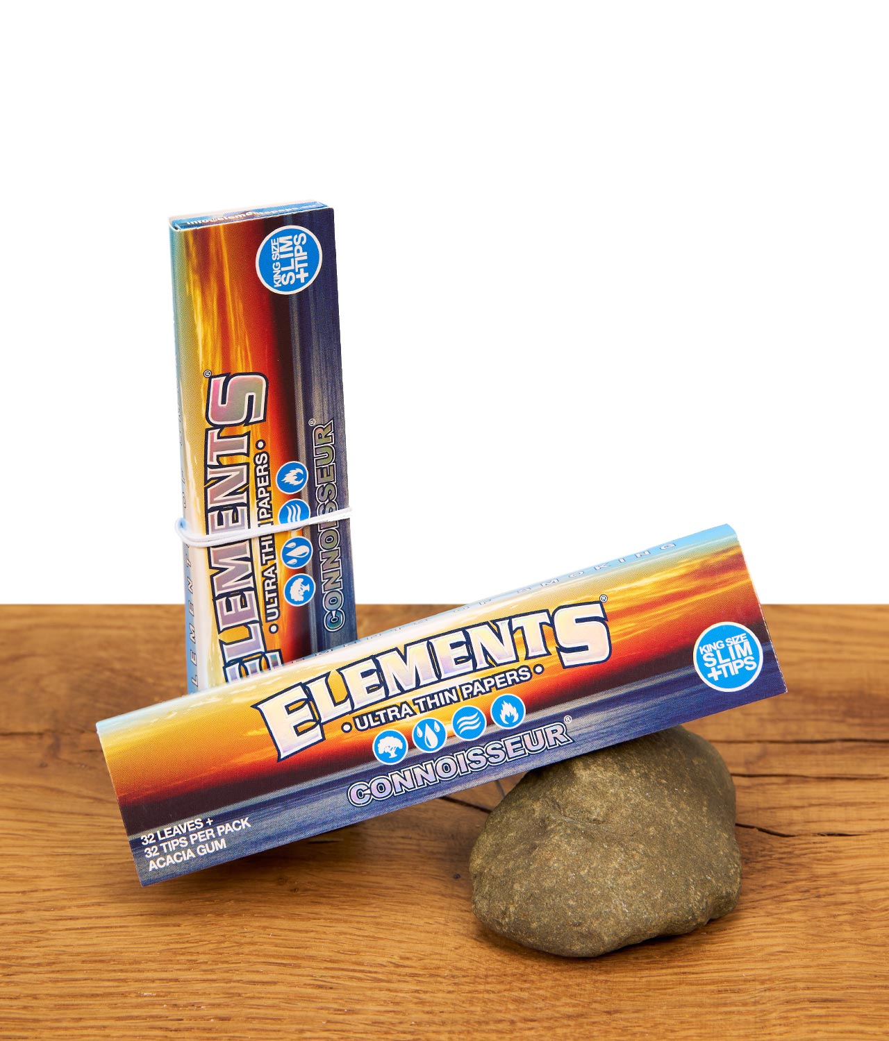elements-connoisseur-ultra-thin-papers-mit-tips-jpg Zwei Packungen Elements Connoisseur King Size Slim Papers mit Tips auf Holzgrund, eine Packung lehnt an einem Naturstein.