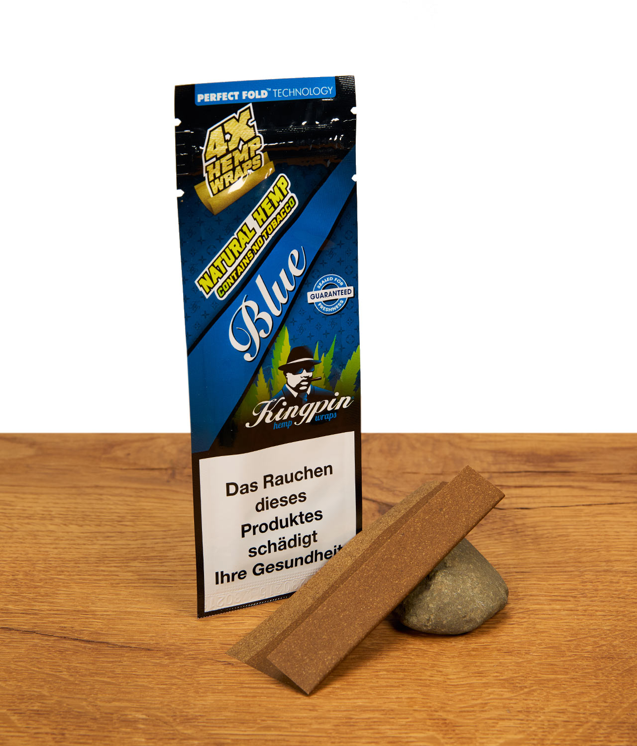 kingpin-hemp-wraps-blue-jpg Kingpin Hemp Wraps Blue Packung mit zwei braunen, tabakfreien Hanf-Blättchen, die an einem Naturstein auf Holz lehnen.