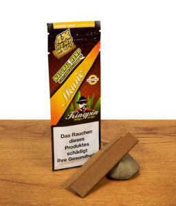 Packung Kingpin Hemp Wraps Manic neben einem einzelnen, vorgefalteten Blunt-Leaf, das auf einem kleinen Stein auf Holz präsentiert wird.