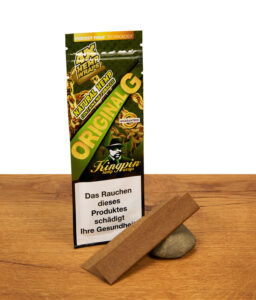 Grüne Packung Kingpin Hemp Wraps Original G mit einem vorgefalteten Naturhanf-Blunt, der dekorativ auf einem Stein auf Holz liegt.