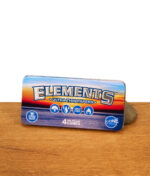 Geschlossene Elements King Size Blechdose mit geprägtem Logo und farbenfrohem Sonnenuntergang-Design auf einem Holzuntergrund.
