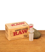 RAW ConeVerter 14mm Adapter aus Borosilikatglas neben der braunen Originalverpackung auf einer Holzoberfläche.
