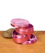 Zerlegter Elements Pink Grinder 4-teilig aus rosafarbenem Aluminium. Gestapelte Einzelteile zeigen den modularen Aufbau.