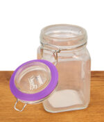 Geöffnetes Juicy Jay’s Aufbewahrungsglas mit lila Gummiring am Glasdeckel und blickdichtem Verschlussmechanismus auf Holzgrund.