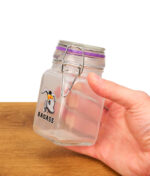 In der Hand gehaltenes Juicy Jay’s Vorratsglas 280ml aus Klarglas mit "Badass"-Esel-Motiv und silbernem Drahtbügelverschluss.