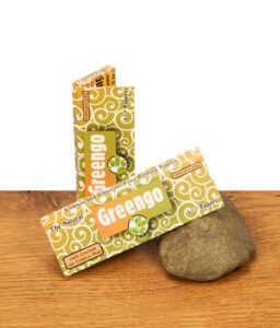 Zwei Packungen Greengo Natura 1 1/4 Size Papers auf einem Holztisch. Die chlorfreien, ungebleichten Blättchen lehnen an einem Stein.