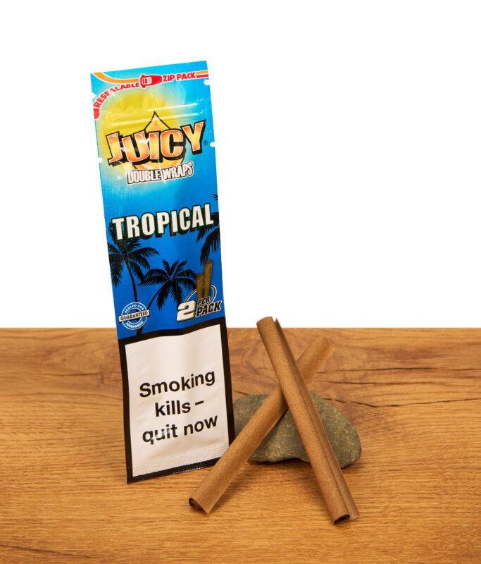 Wiederverschließbares Juicy Double Wraps Tropical Zip-Pack neben zwei gerollten Blunt Wraps auf einem Stein und Holztisch.