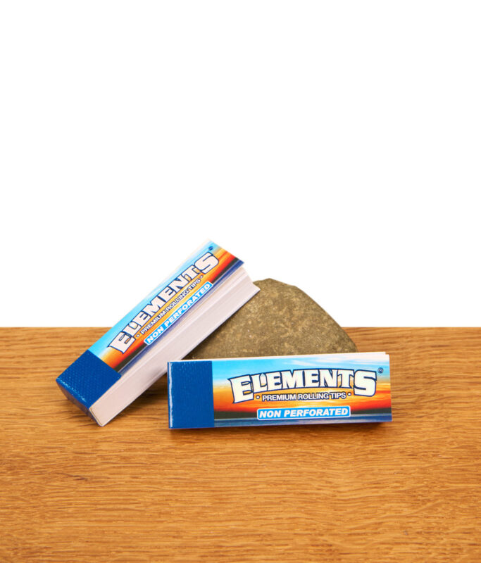 Zwei Booklets Elements Premium Rolling Tips nicht perforiert, drapiert an einem Stein auf einer hellen Holzoberfläche.