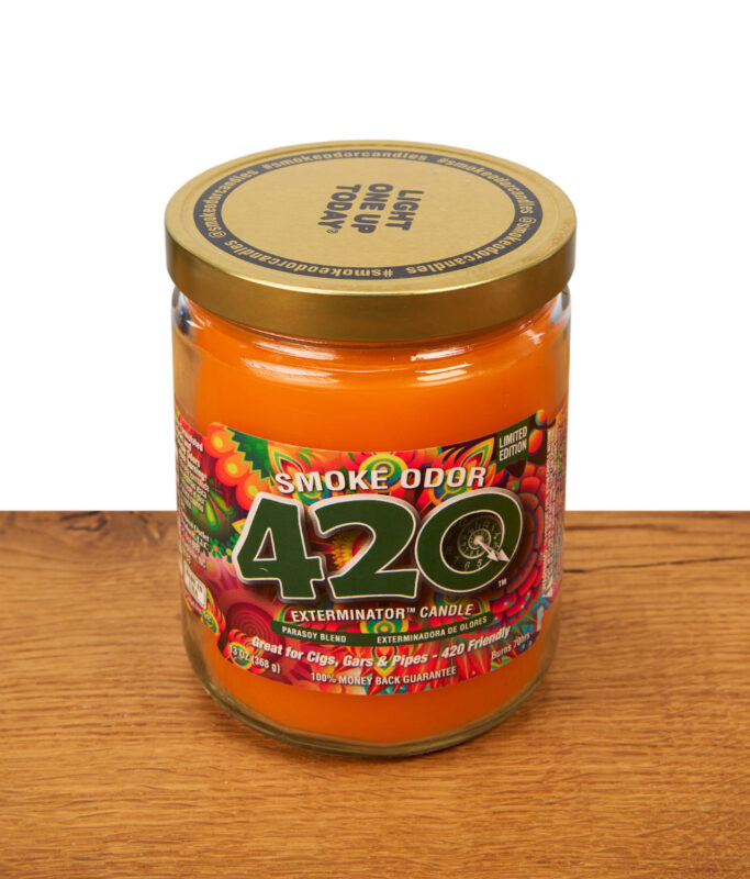 Geschlossene Smoke Odor 420 Exterminator Candle im Glas mit goldenem Deckel auf Holz, orangefarbenes Wachs und farbiges Etikett.