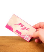 Eine Hand hält ein rosa Päckchen Purize Pink Papes 'n' Tips (King Size Slim) über einem Holztisch.