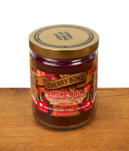 Smoke Odor Exterminator Duftkerze "Cherry Bomb" im 13oz Glas mit goldenem Metalldeckel und dekorativem Etikett auf einer Holzoberfläche.