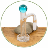 Ein "High Tower" Quarbanger fürs Dabbing mit blauer Murmel und Quarz-Säule im Inneren vor einem Naturstein stehend.