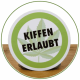 Aufkleber Sticker mit Schrift "Kiffen erlaubt" in grünem Kreis. Perfektes Headshop Lifestyle Produkt auf Holz präsentiert