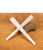 Zwei weiße Cones Black King Size Prerolled aus Papier mit Papp-Filtertip gekreuzt auf einem Stein.