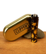 Clipper Metall Leaves Gold Feuerzeug mit schwarzer Kappe neben goldenem Clipper-Etui auf Holz. Schwarzes Metall mit goldenem Hanfblatt-Motiv.
