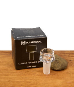 Das gläserne MJ Arsenal Lumina Flower Bowl Köpfchen steht aufrecht vor der Produktbox auf einer Holzoberfläche und zeigt die tiefe Kräuterkammer des NS14 Borosilikatglas-Kopfs.