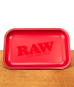 Mattrote RAW Classic Rolling Tray Drehunterlage aus Metall mit dezentem, gleichfarbigem Logo auf einer Holzunterlage.