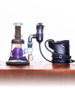 Puffco Peak Pro Link im Onyx-Finish, angeschlossen an eine kunstvolle, farbige Glas-Dab-Rig für ein stationäres E-Dabbing-Erlebnis.