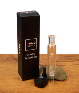 XMax V4 Pro Glass Bubbler neben schwarzer Verpackung. Transparenter Wasserfilter und magnetischer Adapter mit Metallsieb auf Holztisch. Auch mit V3 Pro kompatibel.