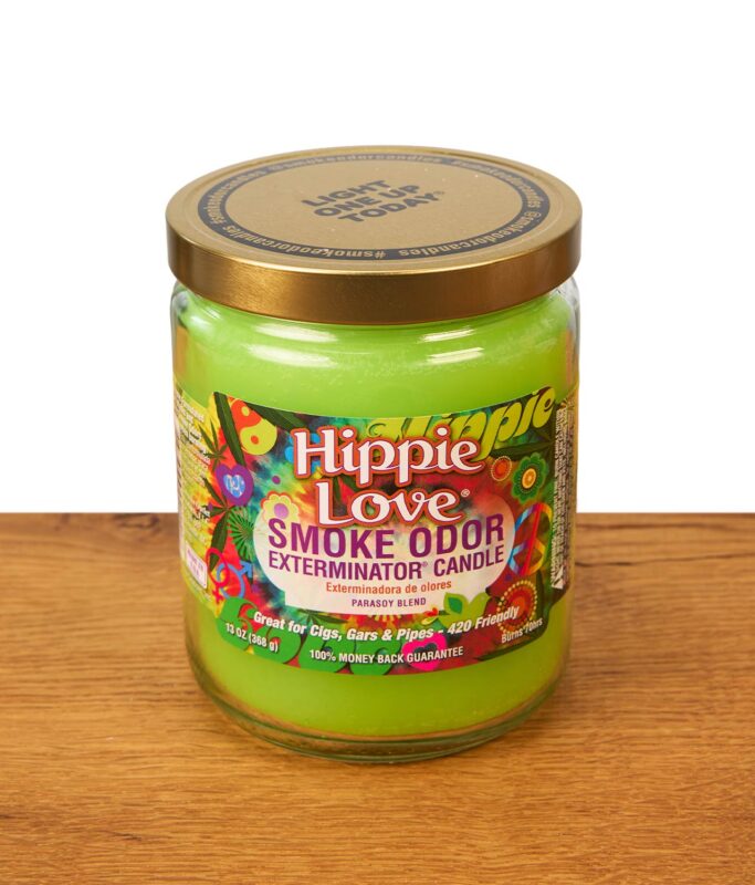 Geschlossene Smoke Odor Exterminator Duftkerze Hippie Love im großen Glas mit farbenfrohem Retro-Etikett und goldenem Schraubdeckel auf einer Holzoberfläche.