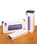 Die drei minimalistischen weißen Produktboxen des Puffco Sapphire Bundle für das Reise-Etui, den Pen und das Heated Loading Tool auf einem Holztisch.
