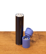 Nahaufnahme der Batterie und Heizkammer des Puffco Pivot Sapphire Edition. Die tiefblaue Silikonkappe ist aufgeklappt und gibt den Blick frei auf die weiße 3D-Heizkammer und den zentralen Luftweg, während das Gerät auf einem Holztisch daneben steht.