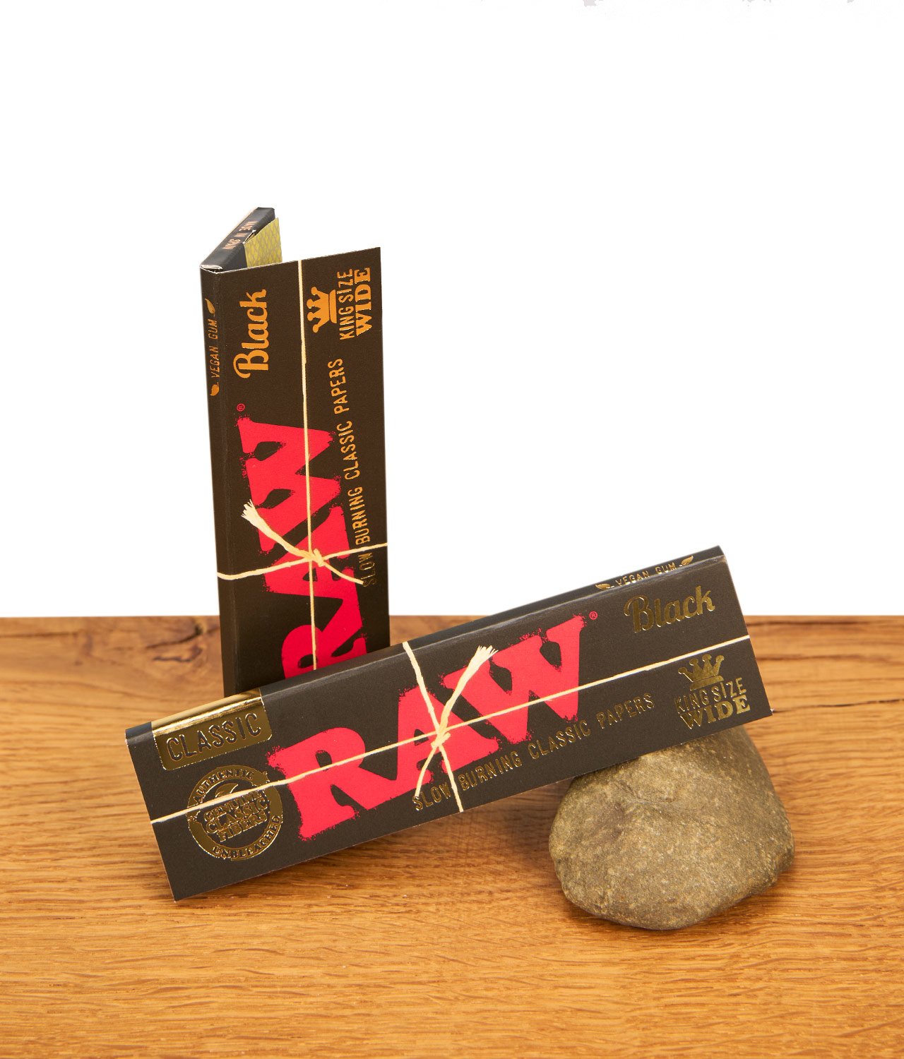 raw-black-king-size-wide-paper-jpg Zwei Päckchen RAW Black King Size Wide Paper. Die schwarzen Heftchen mit rotem Logo und Goldprägung liegen auf Holz und Stein.