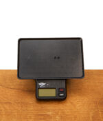 Schwarze Basiseinheit der digitalen RAW Tray Scale Waage mit Kunststoff-Auflagefläche auf einem Holztisch.