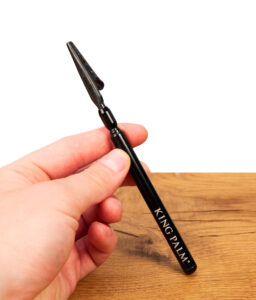 King Palm Blunt Clip aus schwarzem Metall mit weißem Schriftzug, in der Hand gehalten über einer Holzoberfläche.