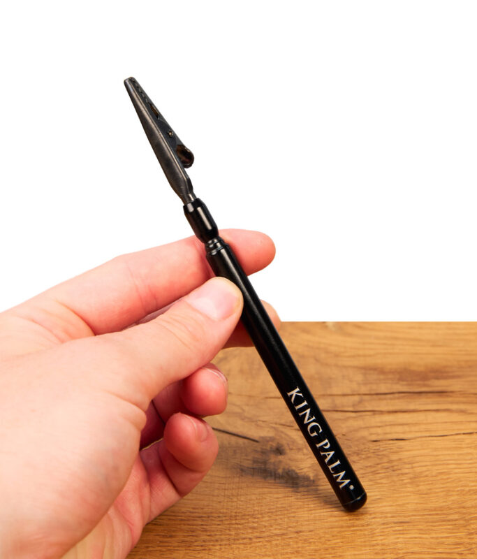 King Palm Blunt Clip aus schwarzem Metall mit weißem Schriftzug, in der Hand gehalten über einer Holzoberfläche.