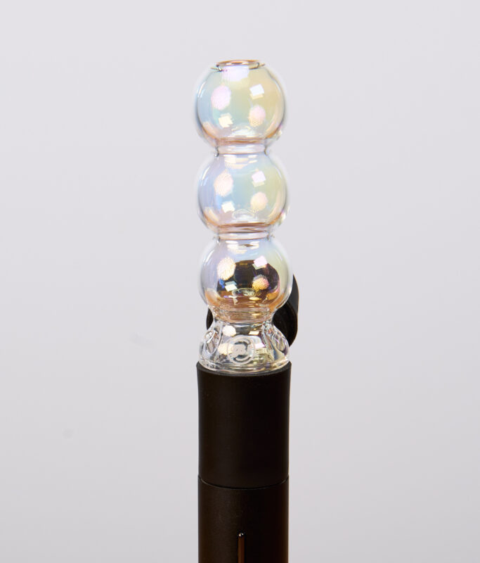 Schimmernder Puffco Pivot Bubble Top Iridescent aus Glas. Der kugelförmige Aufsatz ist passgenau auf den schwarzen Vaporizer aufgesteckt.