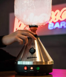 Lifestyle Aufnahme des Volcano Classic Vaporizer mit Dampf in Ballon und LED Schild im Hintergrund