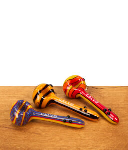 Drei farbenfrohe Calvo Unique Spoon Pipe Glaspfeifen mit Streifenmuster nebeneinander auf Holzoberfläche.