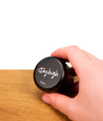 Eine Hand hält den Stayhigh Puck Large aus mattschwarzem Aluminium über einer Holzplatte vor weißem Hintergrund.