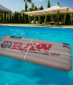 Die beigefarbene RAW Floaty Pack Luftmatratze im authentischen Rolling-Paper-Design schwimmt in einem Pool.