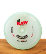 RAW Frisbee Cyan Glow SZN Special Edition: Runde, mintgrüne Kunststoff-Frisbee und Rolling Tray auf einer Holzoberfläche.