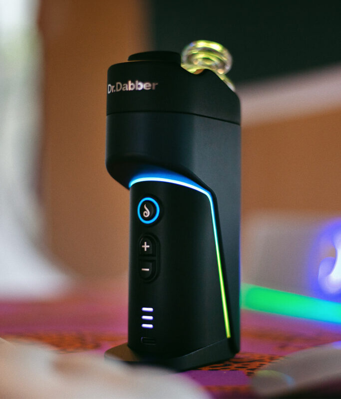 Der Dr. Dabber Switch GO Vaporizer im edlen Indoor-Setup mit blauer und grüner LED-Beleuchtung.
