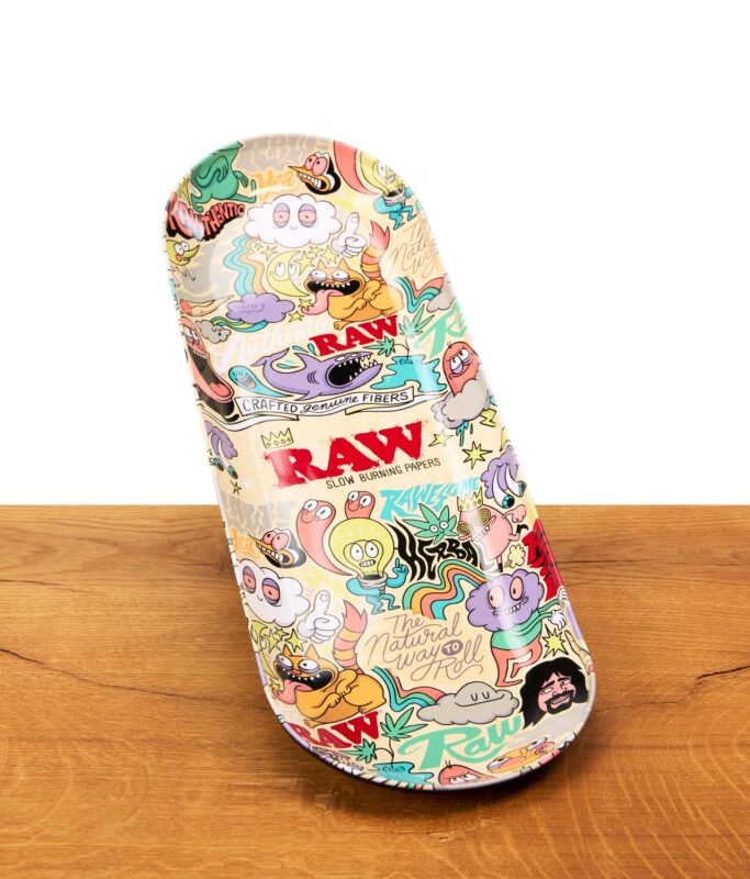 RAW x Chris Psiacik Skate Deck Rolling Tray auf Holzoberfläche, buntes Dreh-Tablett aus Metall in Skateboard-Form.