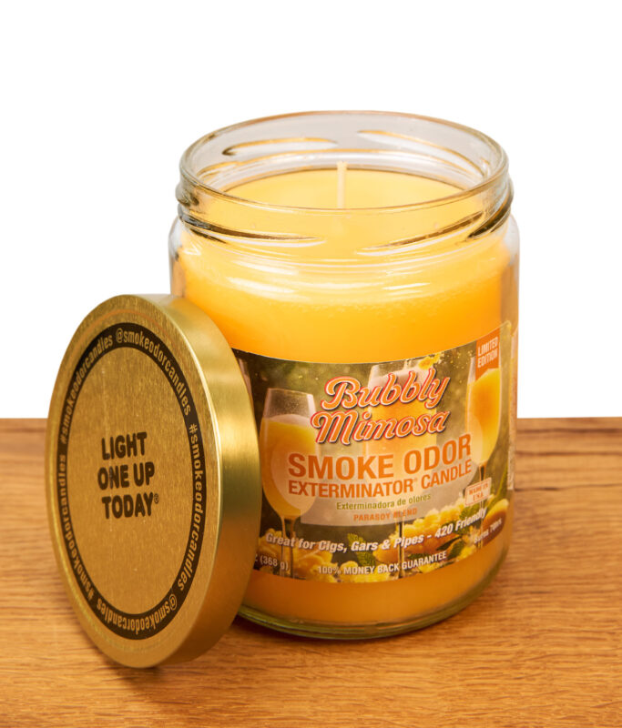 Geöffnete Smoke Odor Bubbly Mimosa Kerze im Glas mit angelehntem goldenen Metalldeckel auf einer Holzoberfläche.