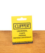 Gelbe Verpackung der Clipper Universal Feuersteine im 9er Pack stehend auf einer hellen Holzoberfläche.